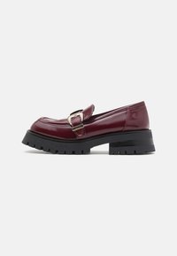 Burgundy patent leather loafers with a rounded toe, adjustable buckle detail, and a thick black treaded sole.