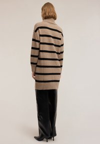 Maglione a maglia beige con strisce orizzontali nere, colletto alto, maniche lunghe e una vestibilità leggermente oversize, abbinato a pantaloni in pelle neri.