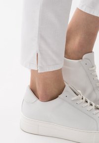 Bílé kalhoty ke kotníkům s bočními rozparky na spodním lemu, spárované s bílými koženými teniskami s kulatou špičkou a plochou podrážkou.