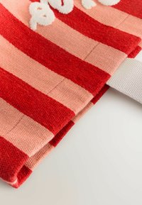 Czerwono-różowa tkanina w paski o teksturowanym wykończeniu. Posiada białą tkaninową zakładkę i puszyste białe litery na pasku.