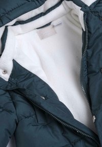 Giacca a vento verde scuro con fodera in morbido pile bianco, zip frontale e chiusure a scatto. Cuciture interne visibili.