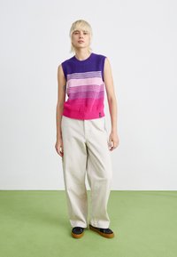 Gebreid mouwloos sweater in paarse en roze gradient met geribbelde zoom; gecombineerd met beige wijde broek en zwarte schoenen.