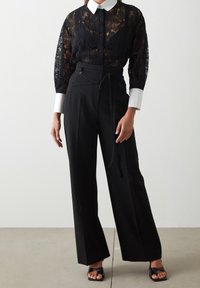 Czarna bluzka z koronką i białym kołnierzykiem, zestawiona z czarnymi spodniami o wysokim stanie z paskiem. Gładkie tekstury, dopasowany krój.
