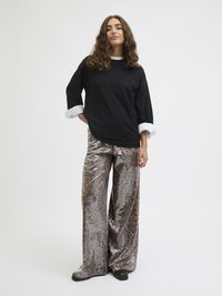 Black oversized long-sleeve top with white cuffs paired with shiny silver sequined wide-leg pants featuring a leopard pattern. Black footwear.