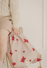 Rosa snorpose med røde sommerfugle- og hindbærmønstre, lavet af blødt stof. Inkluderer et lille logo mærkat på siden.