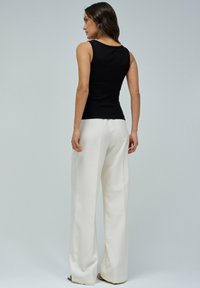 Top sin mangas negro con textura de canalé combinado con pantalones anchos blancos. La parte superior tiene un escote redondo y un diseño ajustado, mientras que los pantalones son suaves con una textura fluida.