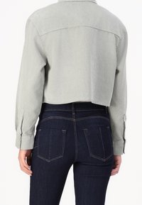 Giacca in corduroy grigia chiara, tagliata, con maniche lunghe e polsini con bottoni, abbinata a jeans a vita alta blu scuro con tasche posteriori.