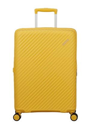 Valigia rigida gialla con scanalature diagonali, quattro ruote nere e manico giallo esteso.