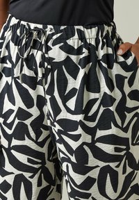 Pantalons à motifs noir et blanc à coupe ample avec une taille élastique et un cordon de serrage, présentant des formes abstraites et un tissu texturé.