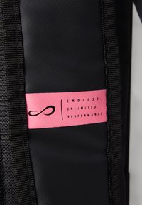 Black backpack material with textured finish features a pink tag displaying “ENDLESS UNLIMITED PERFORMANCE” in black lettering.