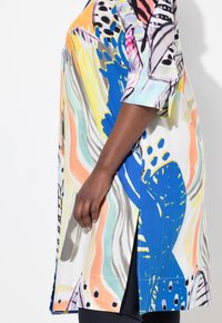 Tunika colorata con motivi astratti nei toni del blu, giallo e rosa, realizzata in tessuto leggero, caratterizzata da uno spacco laterale e maniche corte.