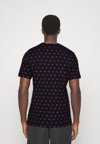 Camiseta negra de manga corta con un patrón repetido de pequeños signos más morados en la parte posterior. La tela parece suave y tiene un diseño de cuello redondo.