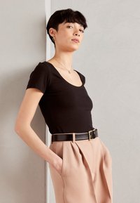 Camiseta negra de escote redondo hecha de una tela suave, combinada con pantalones de talle alto color beige claro y un cinturón negro con hebilla dorada.
