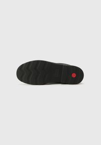 Black sneaker sole with a textured rubber design, featuring a zigzag pattern and a small red circular accent near the heel.