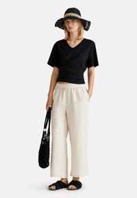 Top corto negro, pantalones sueltos color crema, sombrero tejido negro con una banda beige, bolsa negra y sandalias negras con correas gruesas.