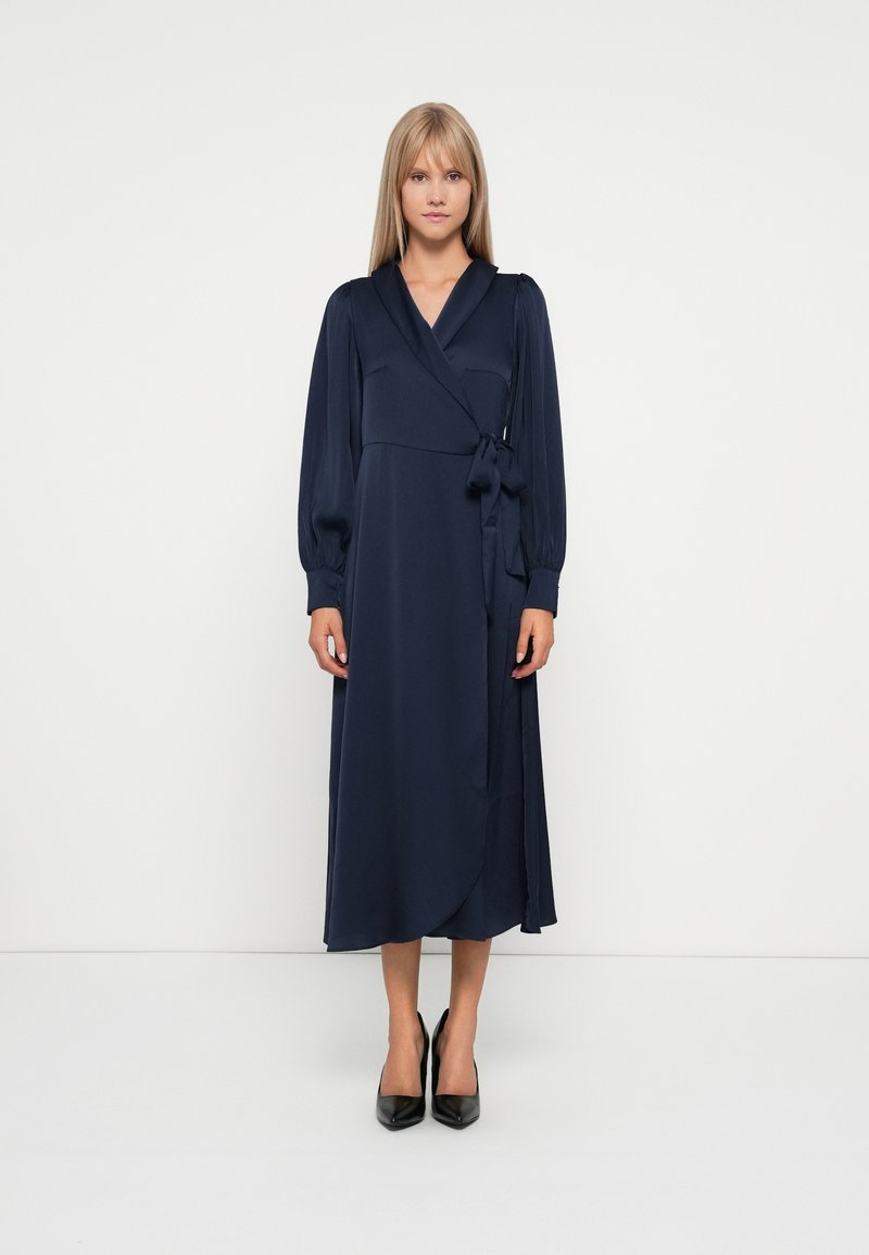 Navy blue wrap dress with long puff sleeves, waist tie detail, and a flowing skirt. Smooth fabric texture, knee-length design.