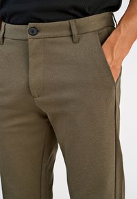 Olijfgroene broek van gestructureerde stof, voorzien van een knoopsluiting, twee zijzakken en een rechte pijpdesign met fijne stikdetails.