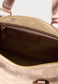 Sac à main rose clair arborant un design avec le logo MK. Texture lisse, accessoires en or et fermeture zippée. L'intérieur présente une doublure marquée et des poches.
