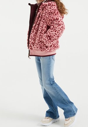 Jakke i pink imiteret pels med sorte leopardpletter, der har lynlås foran, hætte og ribstrikkede ærmegab, kombineret med lyseblå flared jeans og sneakers.
