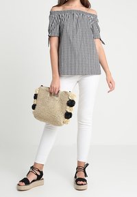 Black and white checked off-shoulder top, white fitted pants, black strappy espadrilles, and a woven beige bag with floral accents.
