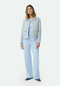 Helles, blaues Tweed-Jackett mit zwei Fronttaschen, kombiniert mit einem hellblauen Oberteil und passenden weit geschnittenen Hosen. Blaue Ballerinas runden das Outfit ab.