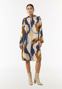 Farbiger Langarmkleid mit Schlüsselloch-Ausschnitt, versehen mit abstrakten Mustern in Blau-, Orange- und Gelbtönen auf einem dunklen Hintergrund.