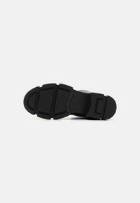 Black shoe sole with a textured surface, featuring multiple grip patterns and a contoured shape. Durable material with a smooth finish.