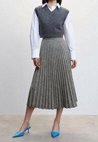 Gonna midi plissettata grigia abbinata a un gilet grigio e una camicia bianca, completata da décolleté blu a punta. Tessuto testurizzato con righe verticali.