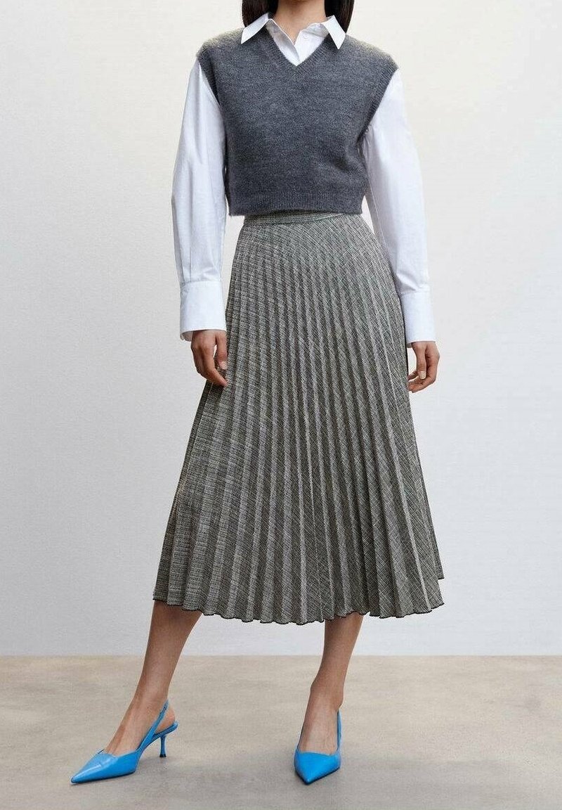 Falda midi plisada gris combinada con un chaleco gris y una camisa blanca, complementada con unos tacones de punta azules. Tejido texturizado con líneas verticales.