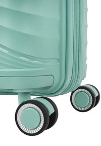 Maleta rígida de color verde azulado con textura ondulada, que cuenta con un cierre de cremallera y dos ruedas negras con acentos plateados para facilitar su movilidad.