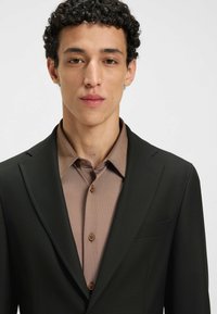 Blazer nero con una finitura testurizzata, abbinato a una camicia button-up beige chiaro con un motivo sottile e bottoni in materiale marrone.