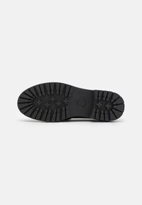 Suola di scarpa in gomma nera con profondi motivi di battistrada per una migliore trazione, dalla forma liscia e arrotondata, con un logo circolare al centro.