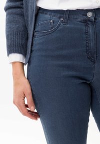 Jean bleu foncé en denim avec une coupe ajustée. Les caractéristiques incluent des poches avant, une fermeture à bouton et des détails de couture subtils.