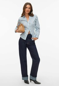 Koszula w paski zapinana na guziki w jasnoniebieskim kolorze, ciemnoniebieskie dżinsy z podwiniętym mankietem oraz brązowa skórzana torebka z detalem w postaci kwiatu na pasku.