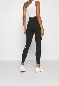 Svarta leggings med hög midja, gjorda av stretchig tyg; har en vit logotypaccent på nederbenet. Kombineras med en vit crop top och sneakers.