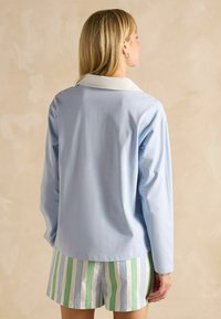 Hele sinine pika varrukaga särk valge kraega, millele on sobitatud triibulised rohelised ja valged lühikesed püksid. Sile kangas ja mugav lõige.