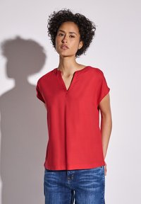 Blusa rossa a maniche corte con scollo a V e vestibilità casual. Tessuto liscio, design minimalista, abbinata a jeans in denim blu.