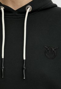 Felpa nera con cappuccio e cordini bianchi, dotata di un piccolo logo ricamato che raffigura due mani che formano un cerchio sul petto.