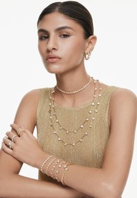 Goldfarbene Schmuckstücke mit geschichteten Halsketten aus klaren Kristallen, Ringen mit kunstvollen Designs und Armbändern mit filigranen Akzenten.
