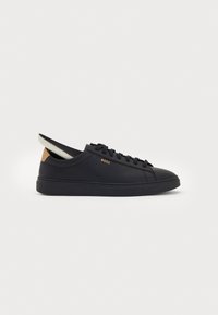 Black low-top leather sneaker with black laces, tan heel tab, and white inner sole, featuring the word "BOSS" in gold on the side.
