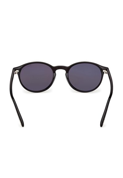 Lunettes de soleil rondes noires avec des verres teintés foncés et des branches fines et courbées, présentées sur un fond blanc.