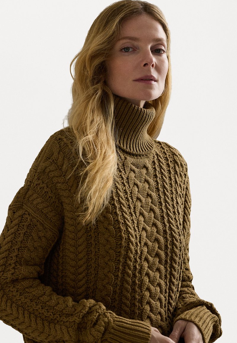Brauner Strickpullover mit einem hohen gerippten Kragen und kunstvollen Zopfstrickmustern. Lange Ärmel mit strukturierten Details.