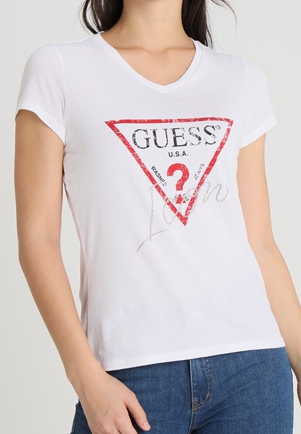 T-shirt blanc à manches courtes avec col en V, arborant un logo et un texte triangulaires rouges et noirs « GUESS », en matériau coton doux.