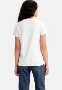 Camiseta de algodón blanca con cuello redondo y mangas cortas, que presenta un corte relajado. Combinada con jeans azules, mostrando un aspecto casual.