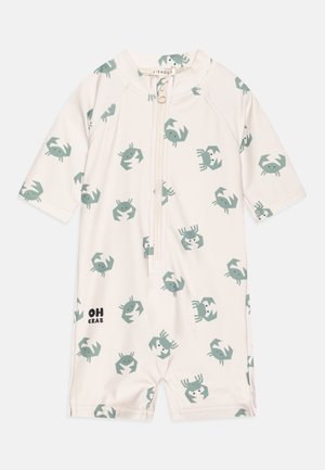 Trumpas rankovėmis, kreminės spalvos vėlės su pakartotiniais krabų raštais muted green atspalviu. Su priekyje esančiu užtrauktuku ir „OH CRAB“ tekstu.