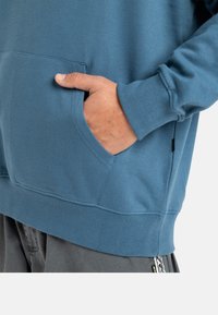 Sweatshirt bleu clair avec une poche kangourou, des poignets côtelés et un ourlet droit. Texture douce et design décontracté.
