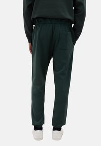 Donkergroene katoenen joggingbroek met een elastische tailleband, zijzakken en geribbelde boorden. Heeft een enkele achterzak.