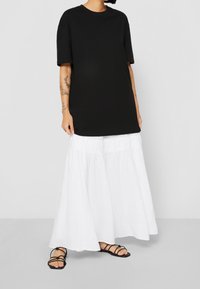 Černé oversize tričko v kombinaci s volnou bílou maxi sukni. Sukně má nařasený pás a jemnou texturu. Celý outfit doplňují černé sandály.