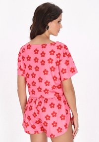 Roze romper met een rood bloemenpatroon, korte mouwen, elastische tailleband en zijsplitten in de short. Glad stoffen textuur.