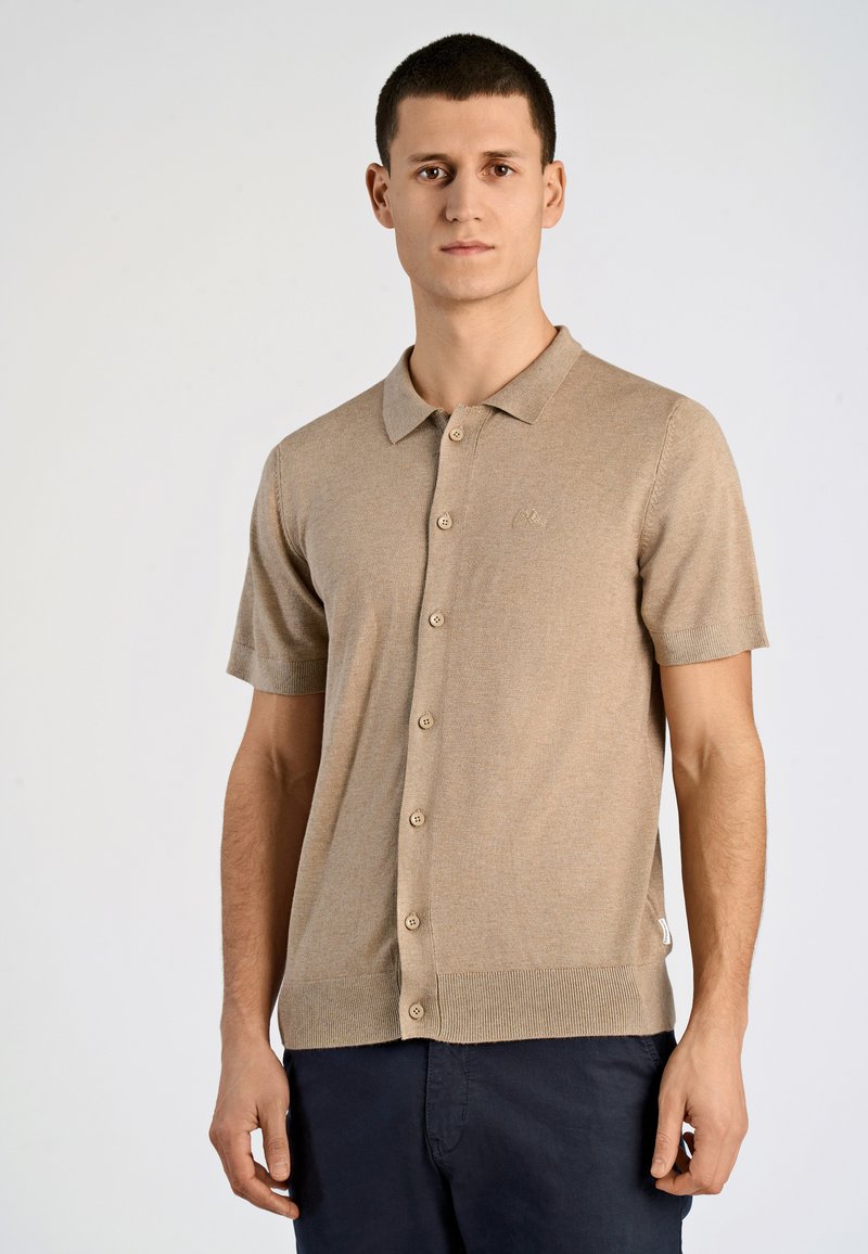 Beige kortärmad polo med knäppning fram, tillverkad av texturerat tyg, med en subtil logotyp på bröstet och ribbad nederkant.